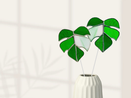 Decorative green leaf-shaped objects in a white vase on a light background