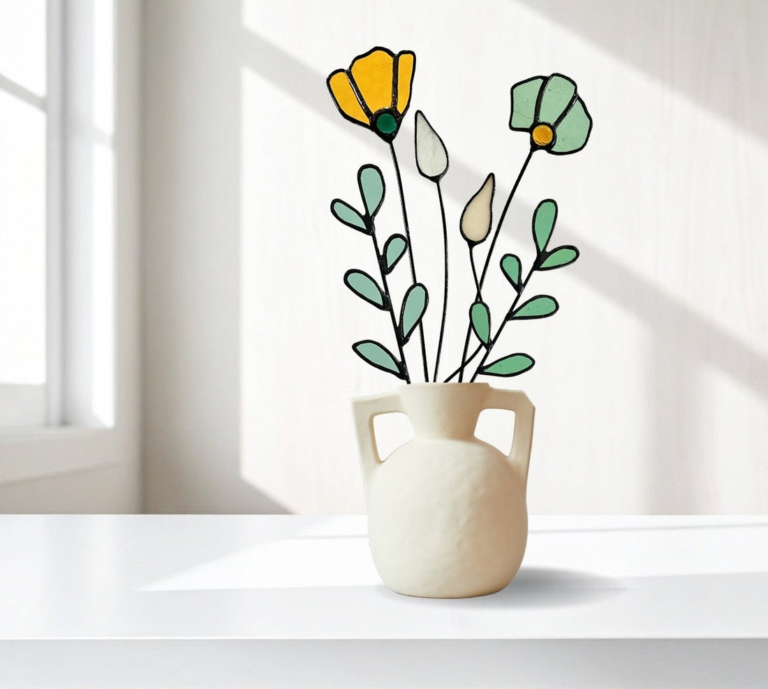 Yellow and mint green glass flowers displayed in a cream vase on a counter top in the sunlight