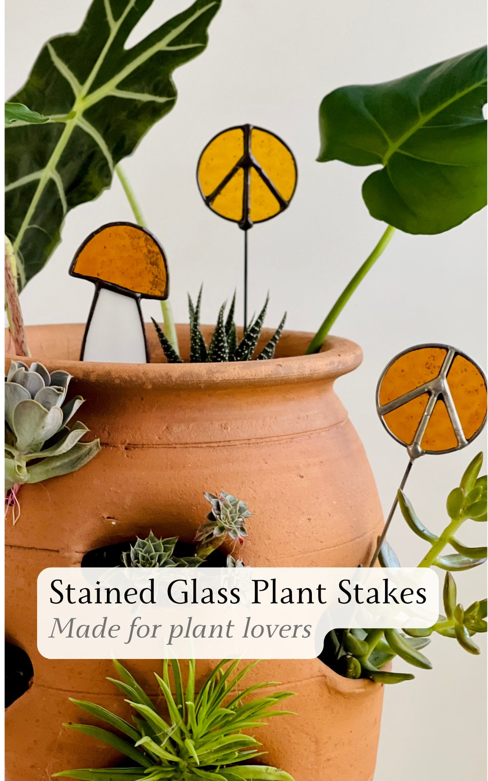 stained glass plant stakes with mushroom and peace sign designs in a terracotta pot with succulents and leafy houseplants