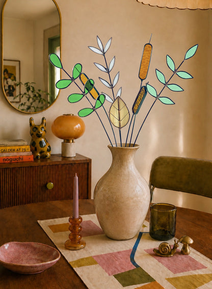 A decorative floral arrangement in a tall cream vase on a dining table, styled in a warm, bohemian room with a mirror, sideboard, candlestick, and small dishes.
