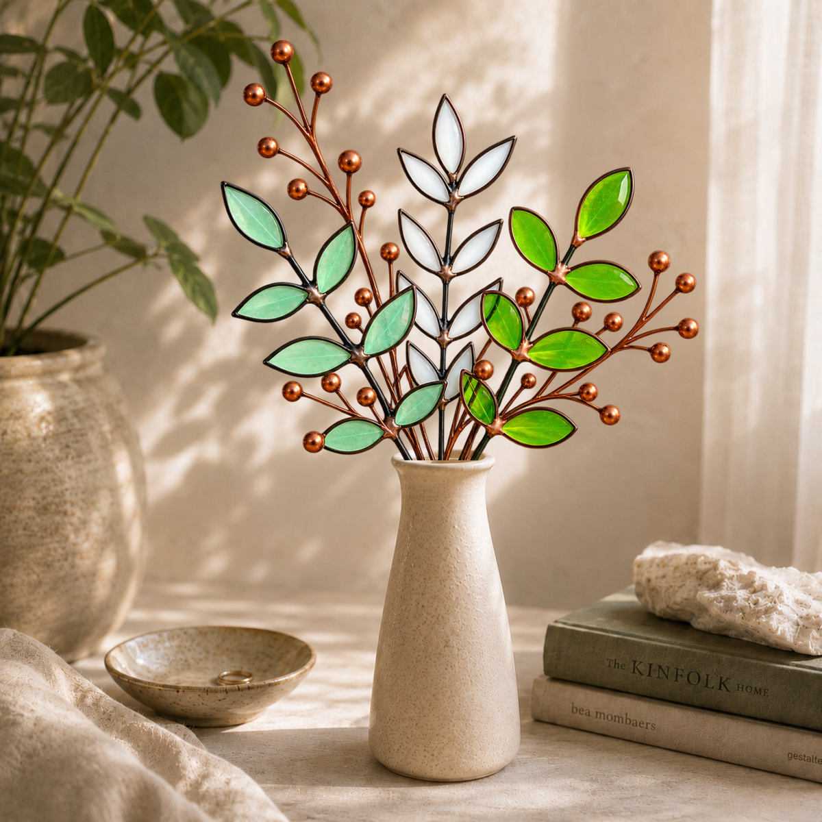 Handmade stained glass botanical arrangement featuring seafoam green, white and bright green glass leaves accented with sculptural copper berry branches, displayed in a cream ceramic vase.