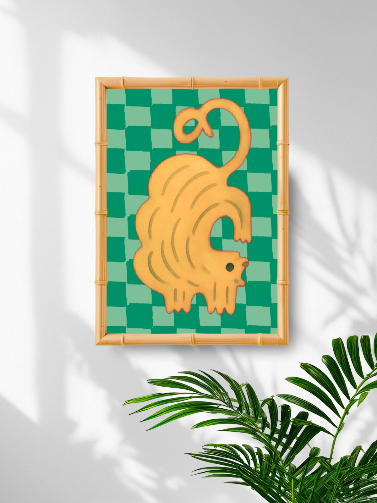 Framed artwork of a yellow cat on a green checkered background with plant leaves in the corner.