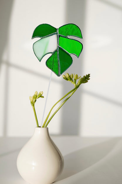 Green leaf-shaped object in a white vase against a light background